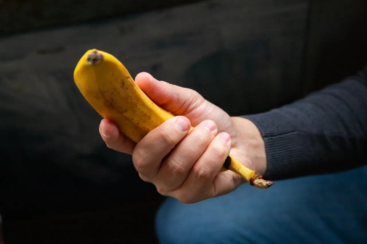 Man holding an unpeeled banana as a visual metaphor for adult phimosis 