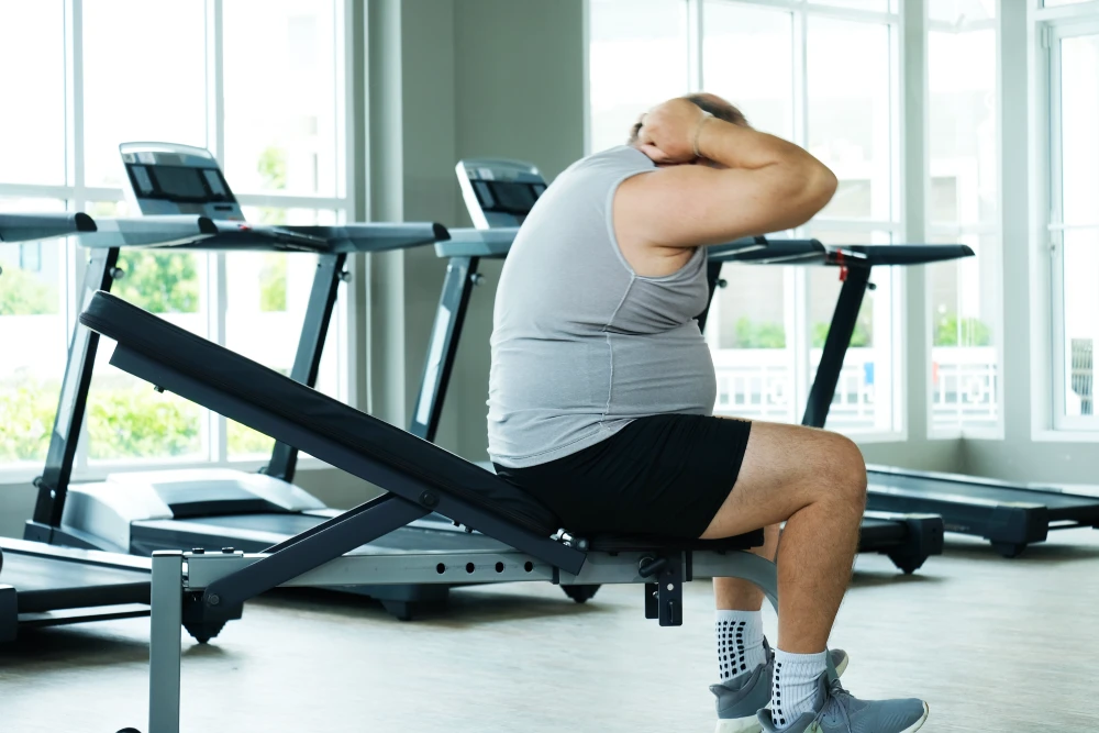 An overweight man exercising at the gym as part of a weight loss management programme.